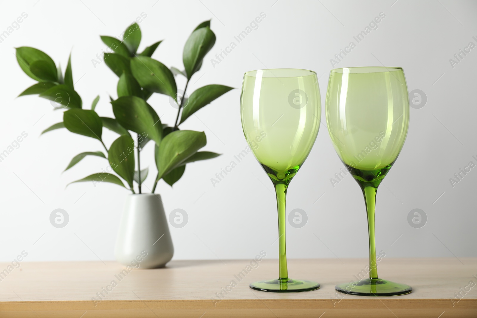 Photo of Two empty clean glasses and vase with leaves on wooden table