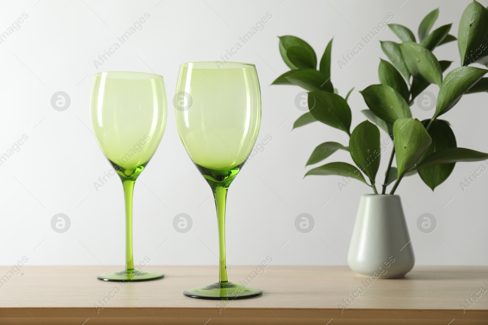 Photo of Two empty clean glasses and vase with leaves on wooden table