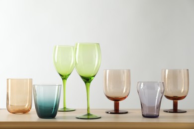 Photo of Many different glasses on wooden table against light background