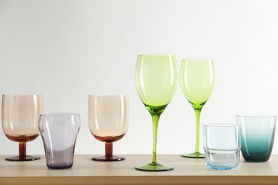 Photo of Many different glasses on wooden table against light background