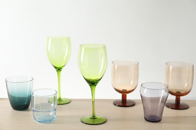 Photo of Many different glasses on wooden table against light background