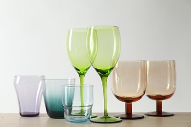 Photo of Many different glasses on wooden table against light background