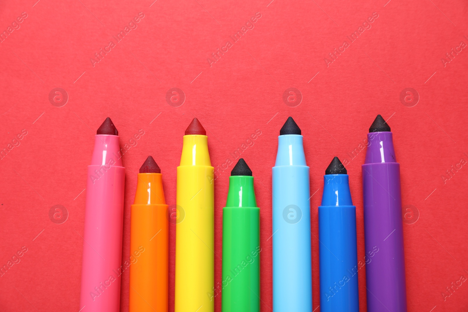 Photo of Many colorful markers on red background, flat lay