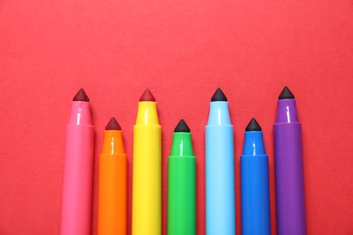 Photo of Many colorful markers on red background, flat lay
