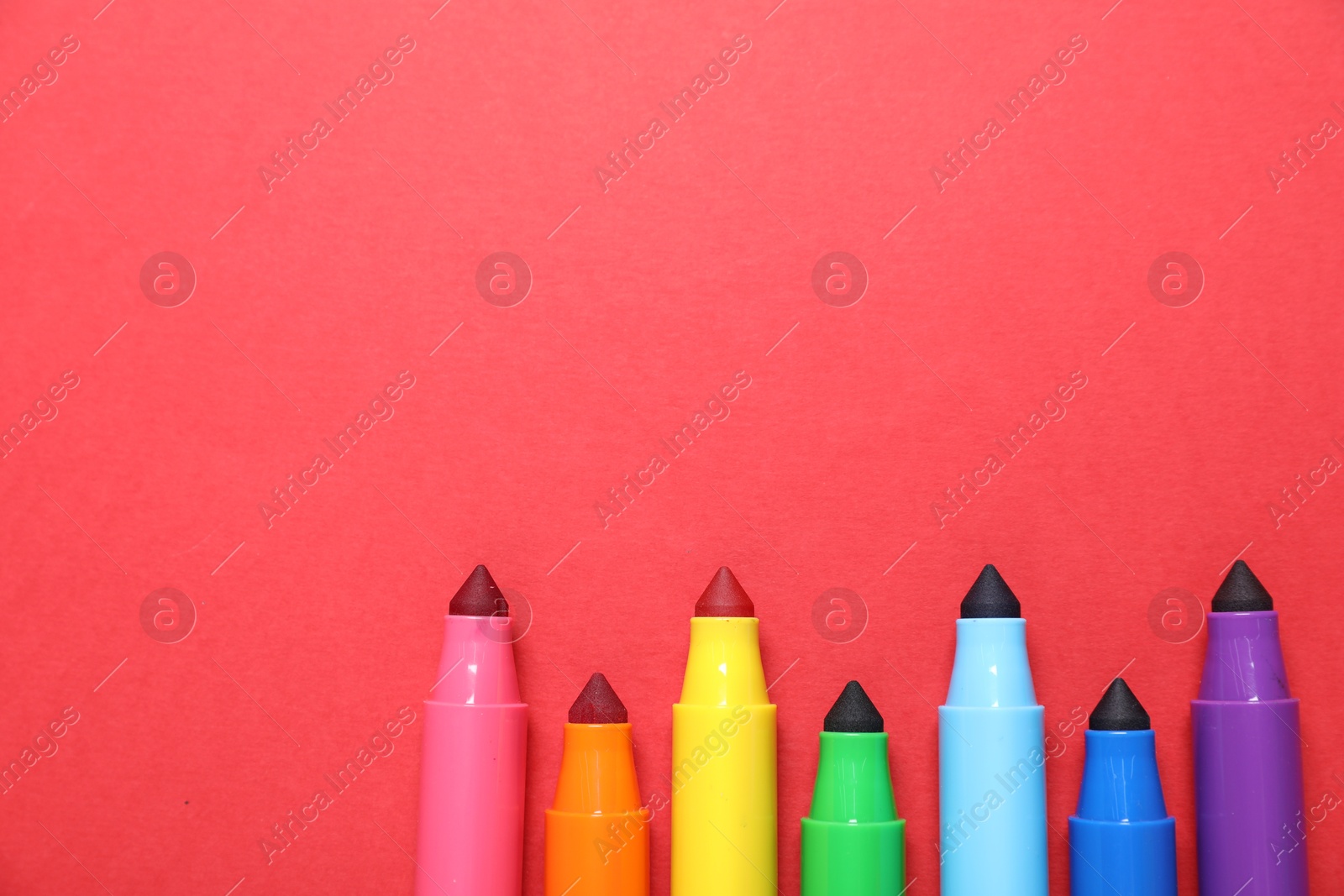 Photo of Many colorful markers on red background, flat lay. Space for text