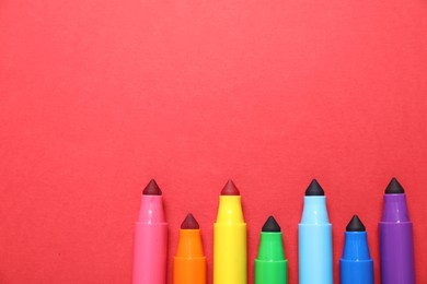 Photo of Many colorful markers on red background, flat lay. Space for text