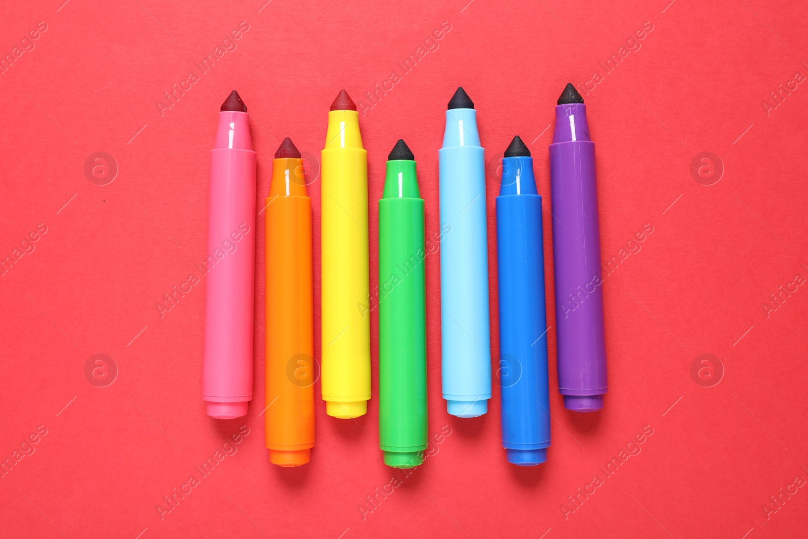 Photo of Many colorful markers on red background, flat lay