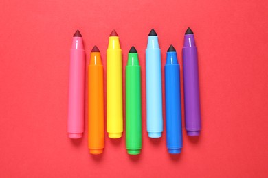 Photo of Many colorful markers on red background, flat lay