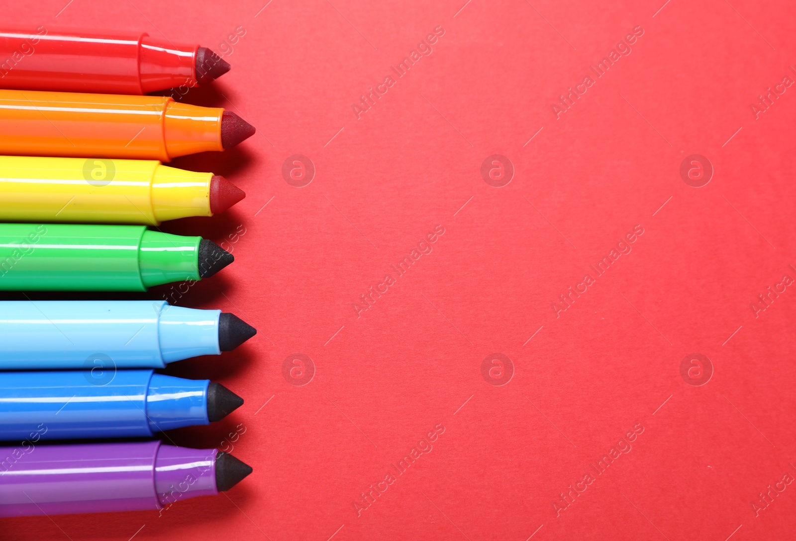 Photo of Many colorful markers on red background, flat lay. Space for text