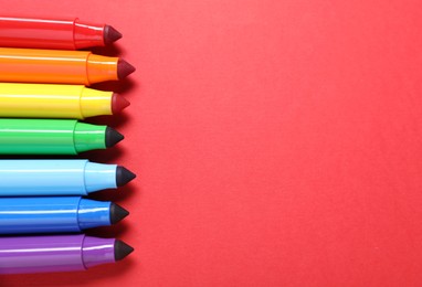 Photo of Many colorful markers on red background, flat lay. Space for text