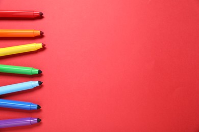 Photo of Many colorful markers on red background, flat lay. Space for text