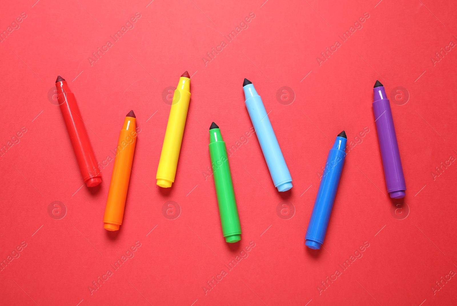 Photo of Many colorful markers on red background, flat lay