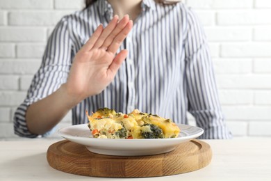 Photo of Woman refusing to eat piece of casserole at table, closeup