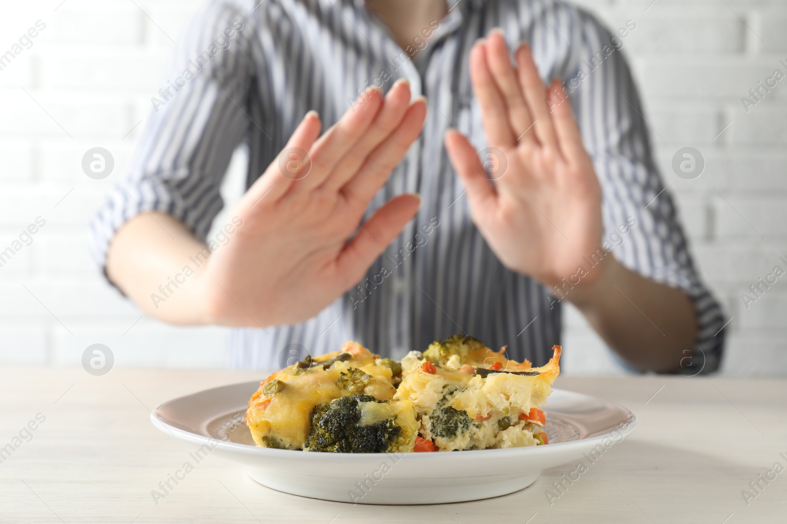 Photo of Woman refusing to eat piece of casserole at table, closeup