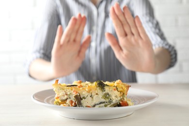 Photo of Woman refusing to eat piece of casserole at table, closeup