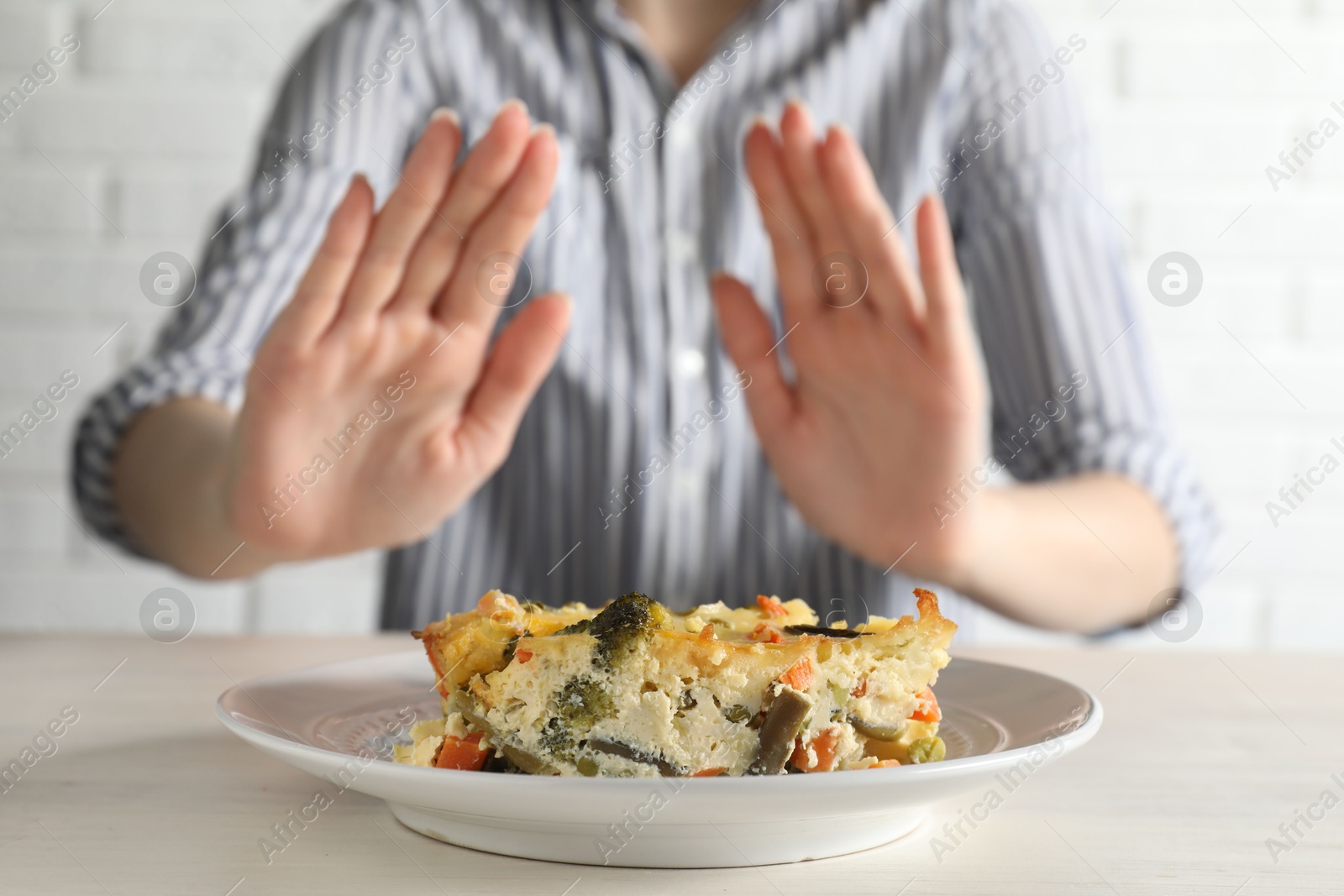 Photo of Woman refusing to eat piece of casserole at table, closeup