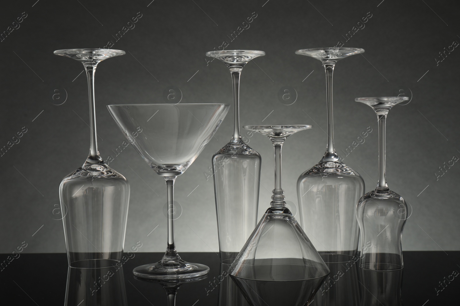 Many empty clean glasses on mirror surface against grey background Photo of Many empty clean glasses on mirror surface against grey background