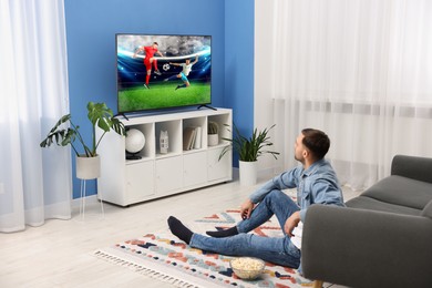 Image of Man watching soccer game on TV set at home