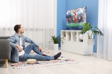 Image of Man watching soccer game on TV set at home