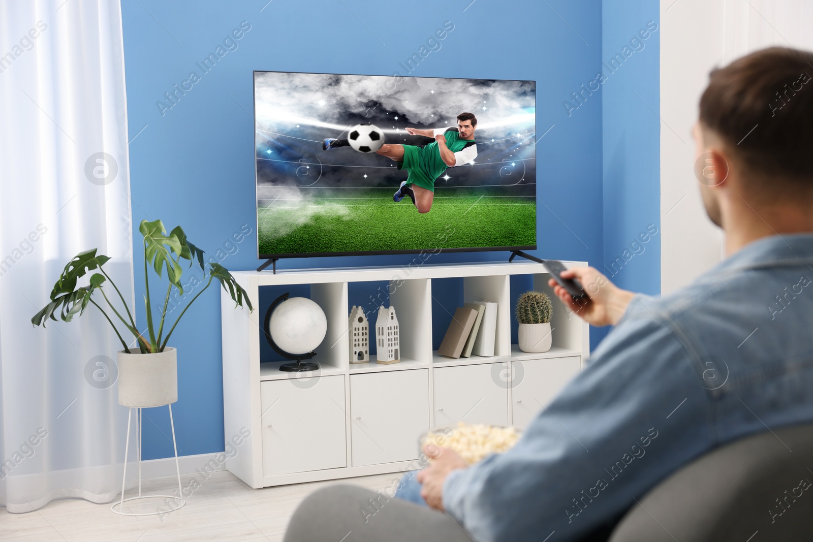 Image of Man watching soccer game on TV set at home