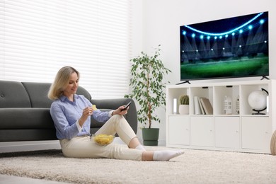 Image of Woman eating chips while watching sport game on TV set at home