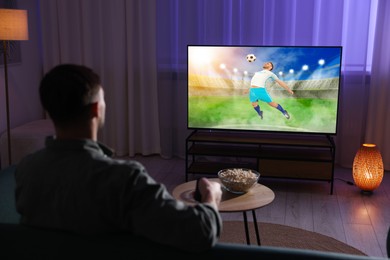 Image of Man watching soccer game on TV set at home