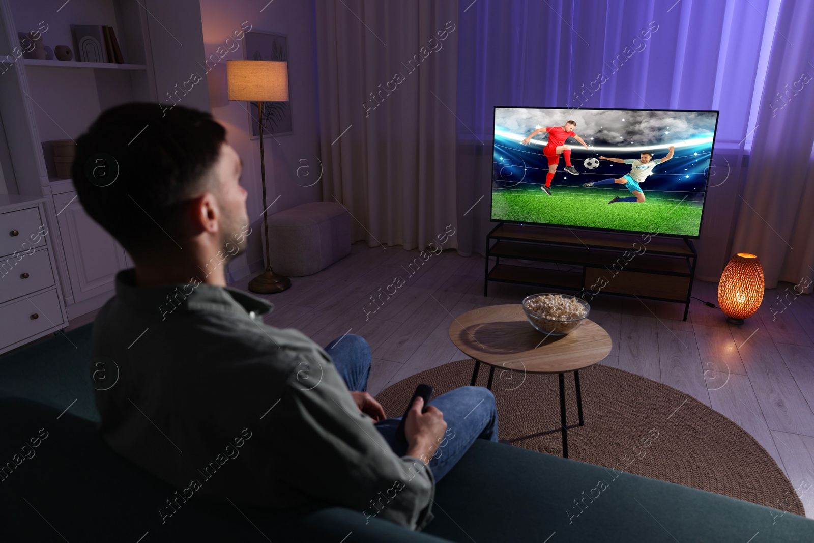 Image of Man watching soccer game on TV set at home