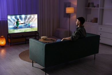 Image of Man watching soccer game on TV set at home