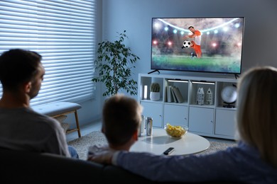 Image of Family watching soccer game on TV set at home