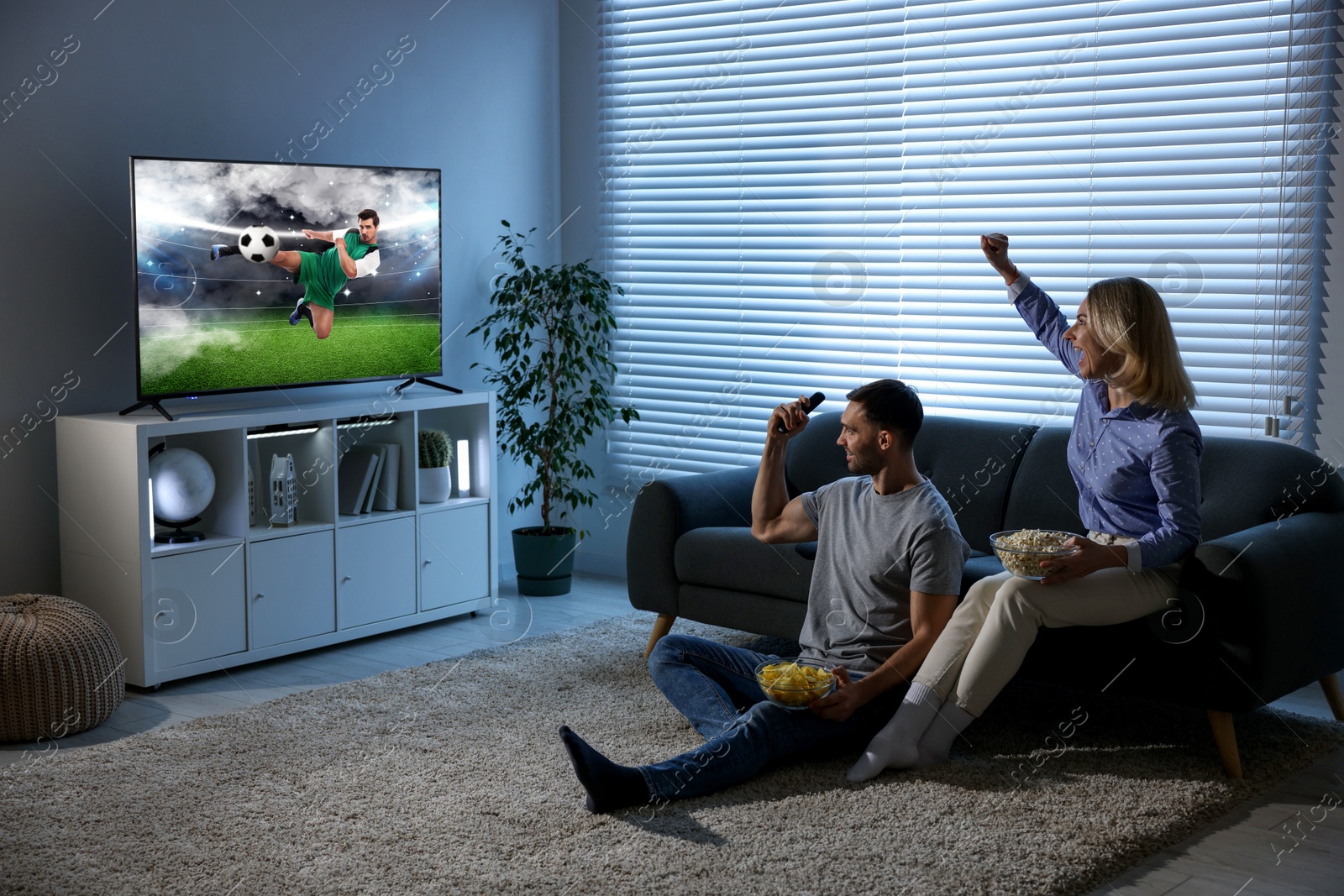 Image of Couple watching soccer game on TV set at home