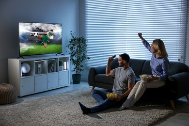 Image of Couple watching soccer game on TV set at home