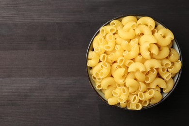 Photo of Raw horns pasta in bowl on dark wooden table, top view. Space for text