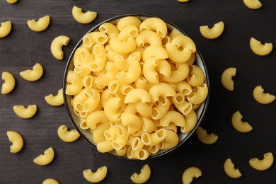 Photo of Raw horns pasta in bowl on dark wooden table, top view