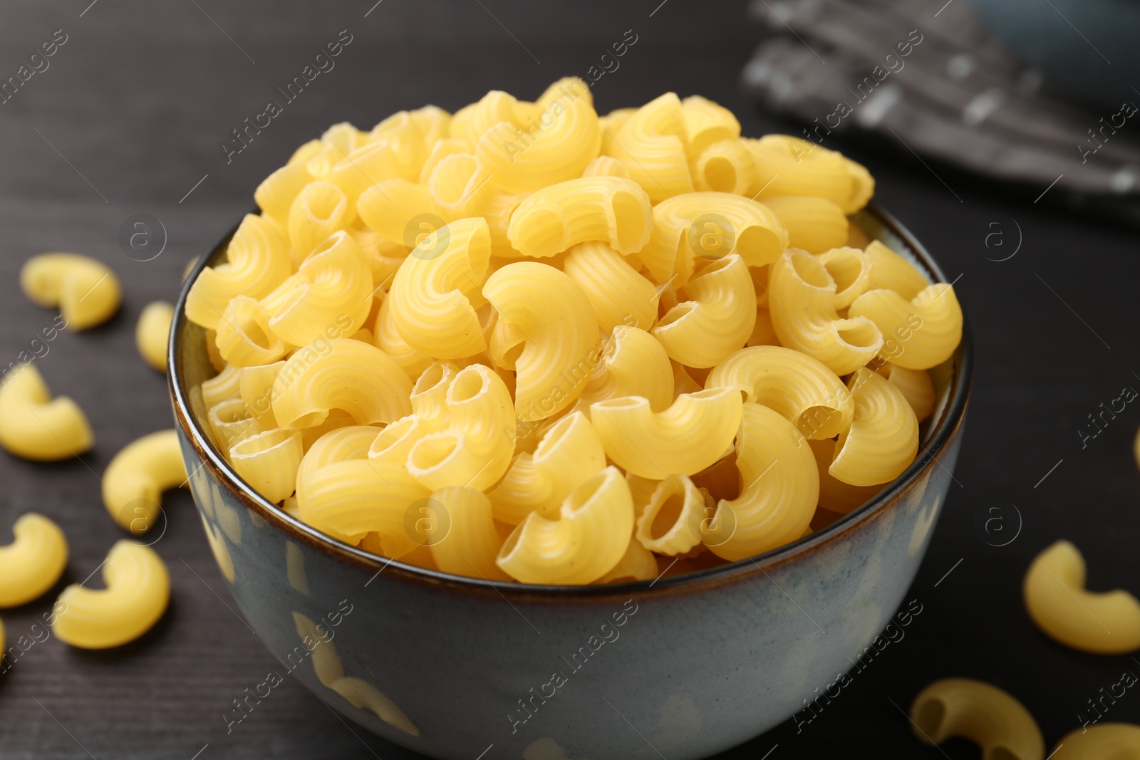 Photo of Raw horns pasta in bowl on dark table, closeup