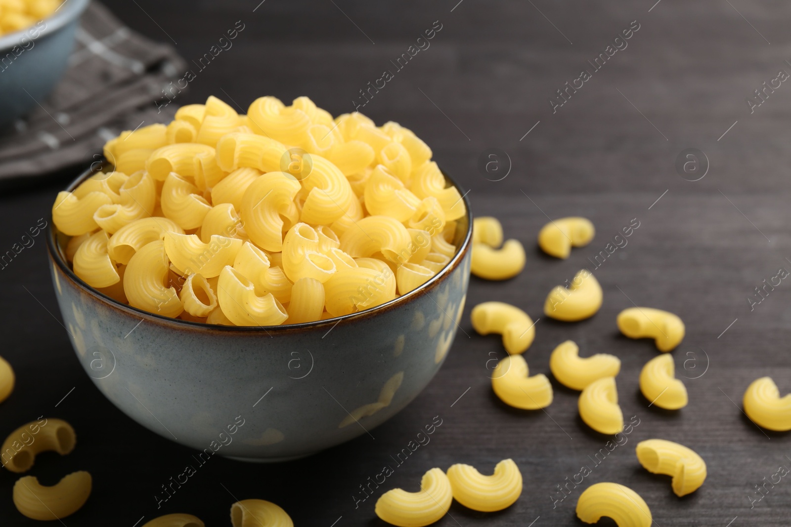 Photo of Raw horns pasta in bowl on dark table, closeup