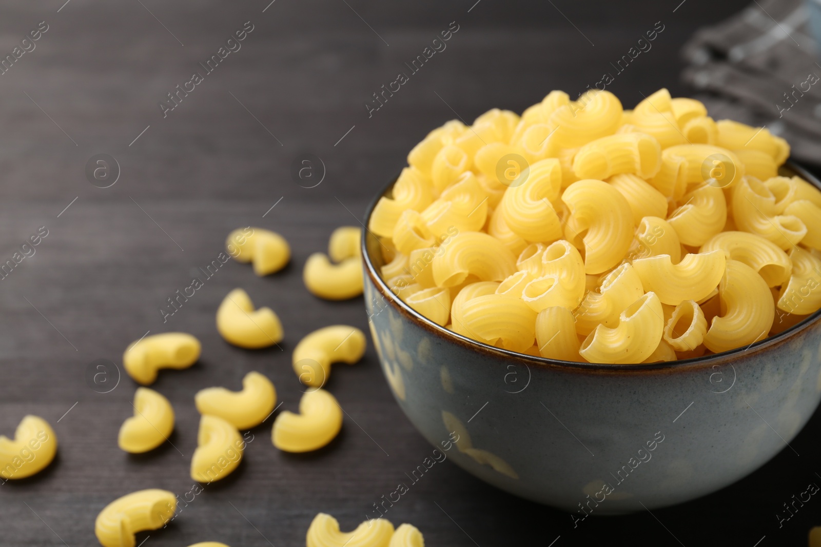 Photo of Raw horns pasta in bowl on dark table, closeup. Space for text