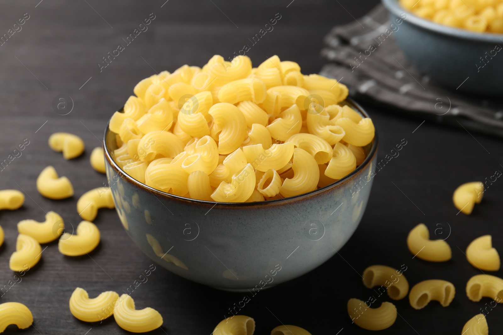 Photo of Raw horns pasta in bowl on dark wooden table, closeup