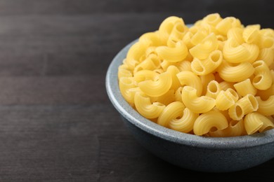 Photo of Raw horns pasta in bowl on dark wooden table, closeup. Space for text