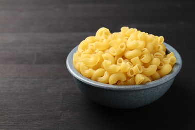 Photo of Raw horns pasta in bowl on dark wooden table, closeup. Space for text