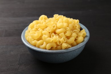 Photo of Raw horns pasta in bowl on dark wooden table, closeup