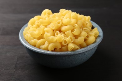 Photo of Raw horns pasta in bowl on dark wooden table, closeup