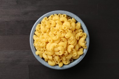 Photo of Raw horns pasta in bowl on dark wooden table, top view.