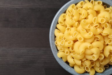 Photo of Raw horns pasta in bowl on dark wooden table, top view. Space for text