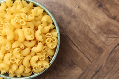 Photo of Raw horns pasta in bowl on wooden table, top view. Space for text