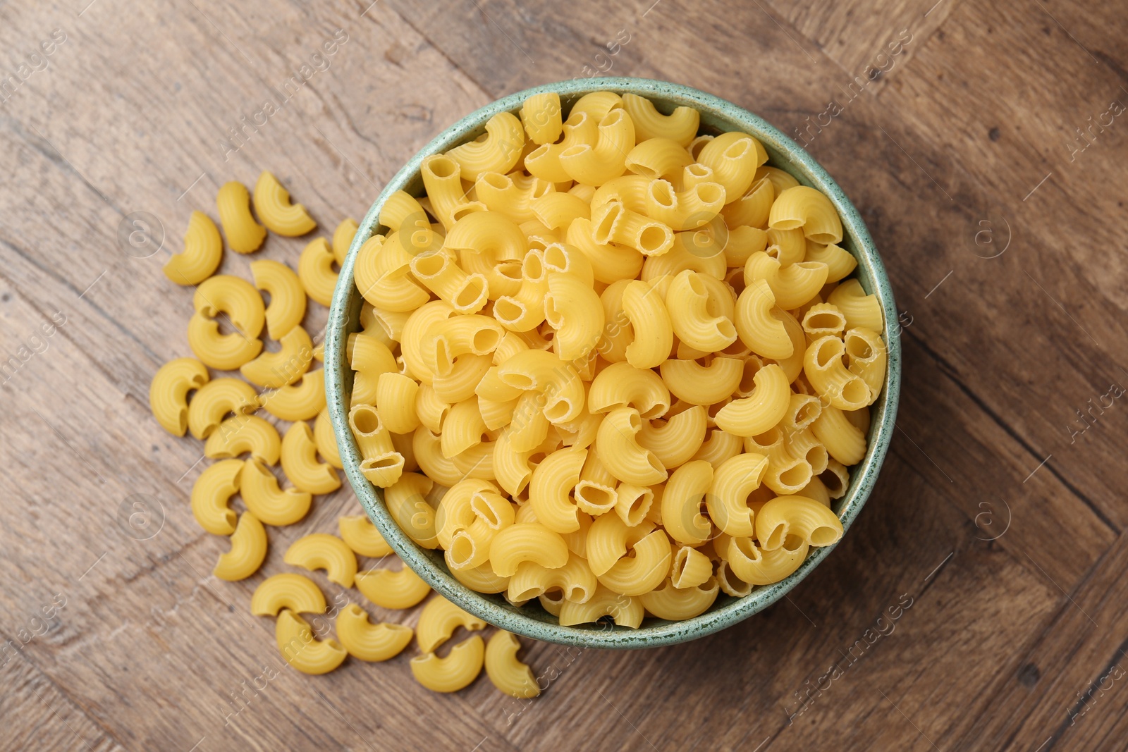 Photo of Raw horns pasta in bowl on wooden table, top view