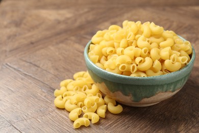 Photo of Raw horns pasta in bowl on wooden table, closeup. Space for text