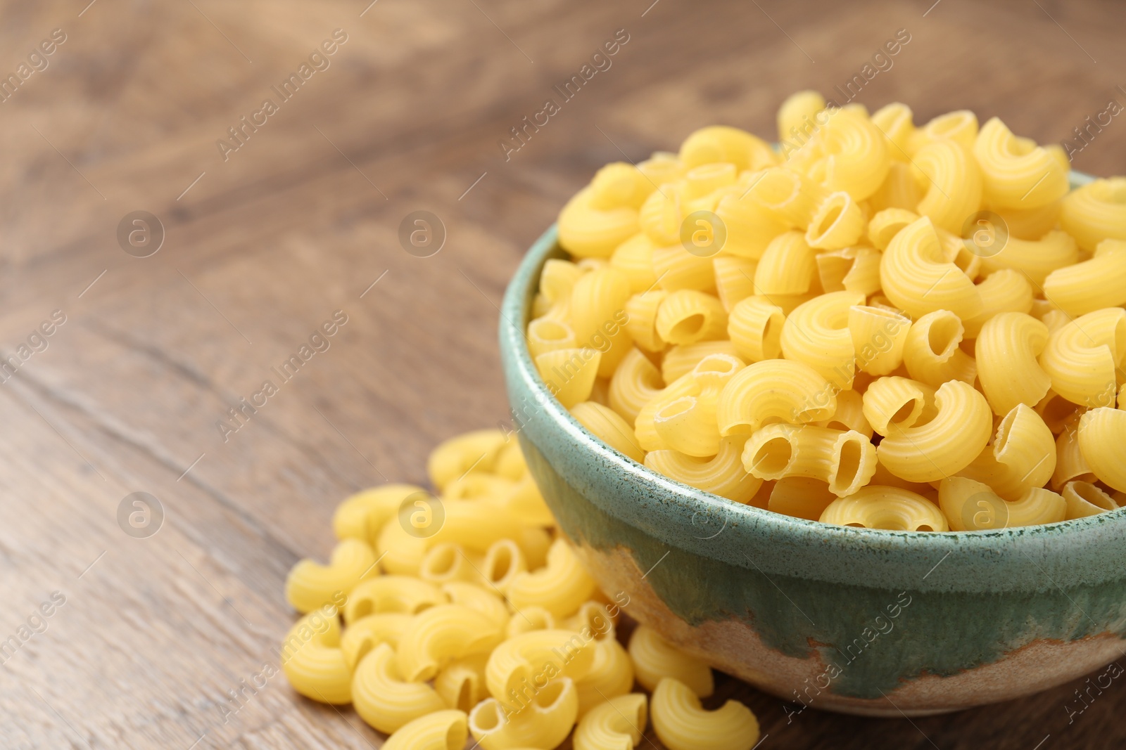 Photo of Raw horns pasta in bowl on wooden table, closeup. Space for text