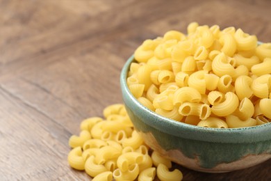 Photo of Raw horns pasta in bowl on wooden table, closeup. Space for text