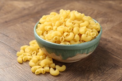 Photo of Raw horns pasta in bowl on wooden table, closeup