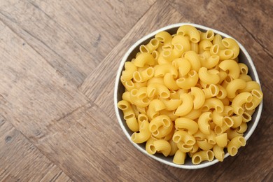 Photo of Raw horns pasta in bowl on wooden table, top view. Space for text